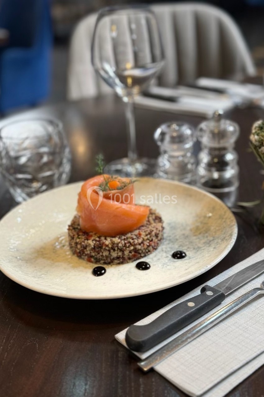Assiette de saumon fumé sur lit de quinoa, décorée de sauce balsamique, servie sur une table dressée élégamment.