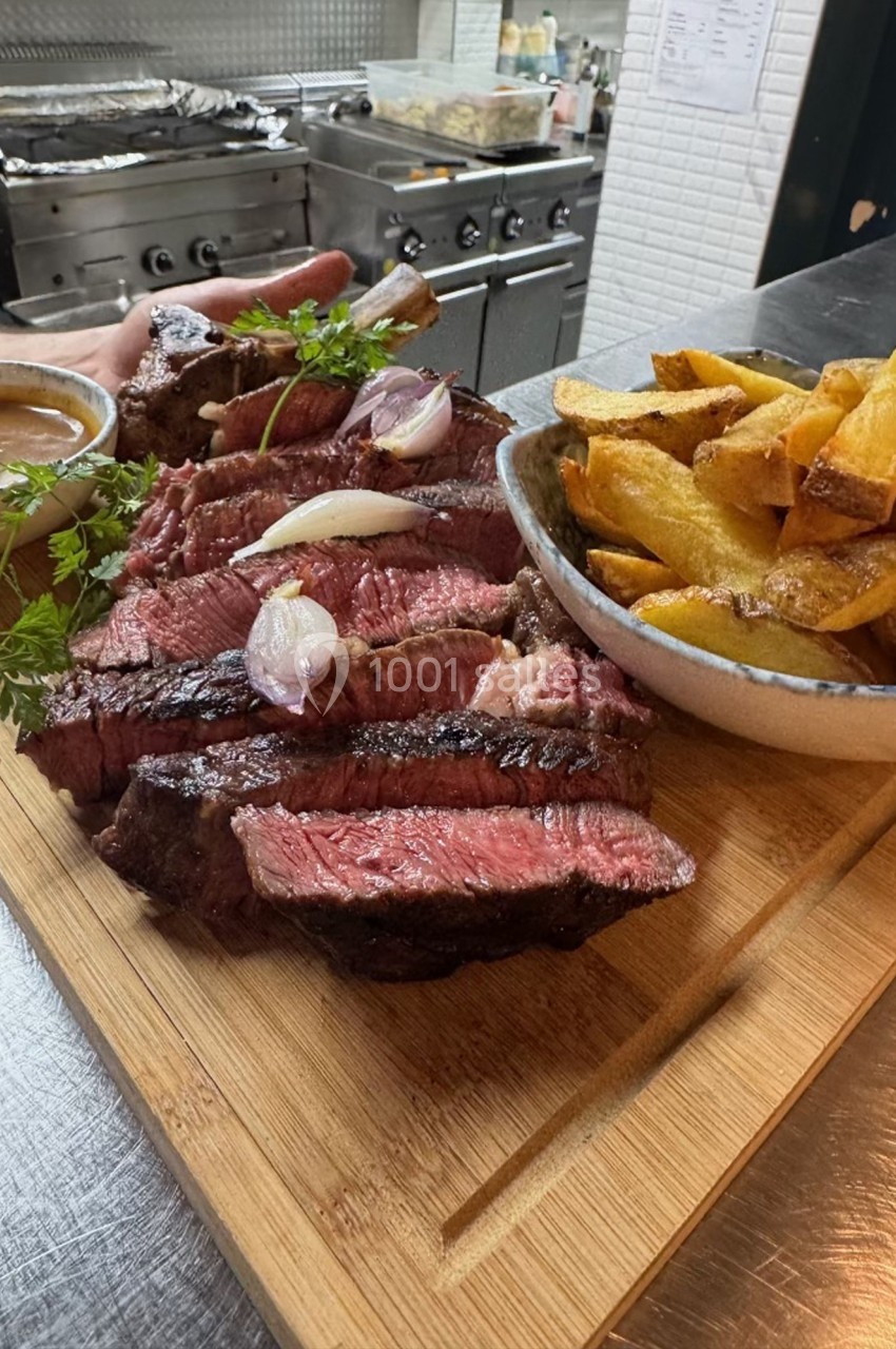 Planche de viande grillée tranchée avec oignons, sauce et frites dorées servies dans un bol, en cuisine.