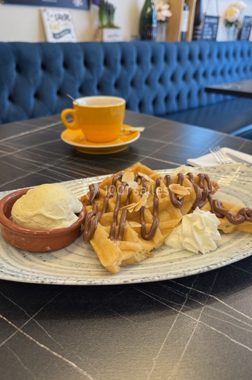 Assiette de gaufres nappées de chocolat avec boule de glace vanille et chantilly, servie sur une table de café.