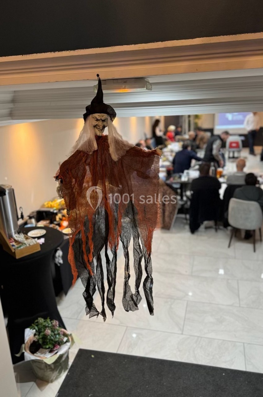 Décoration de sorcière suspendue dans une salle lumineuse où des personnes sont rassemblées autour de tables.