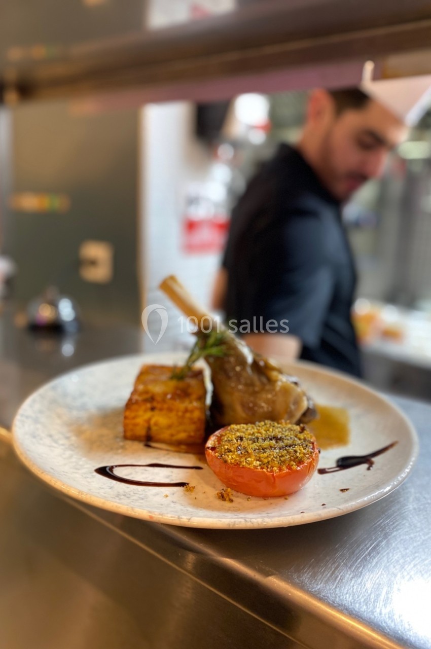 Assiette gastronomique avec un jarret d'agneau, un gratin carré, une tomate garnie et un filet de sauce, en cuisine.