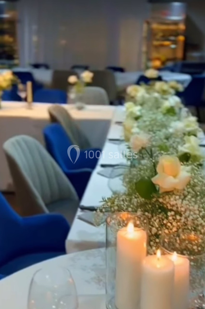 Salle de réception élégamment décorée avec des tables ornées de roses blanches, gypsophiles et bougies allumées.