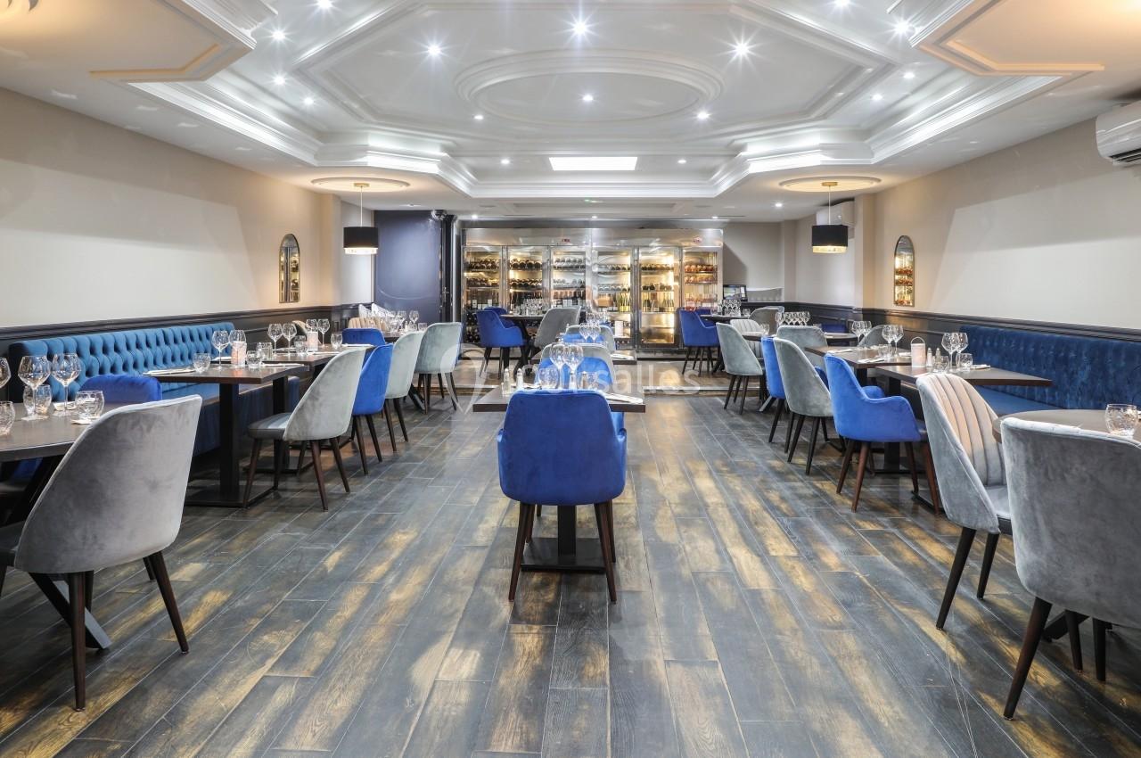 Salle de restaurant élégante avec tables dressées, chaises rembourrées et éclairage tamisé sous un plafond décoratif.