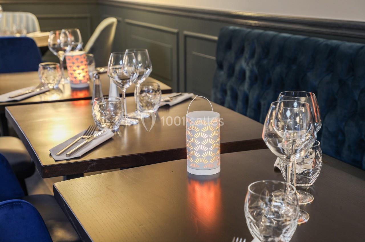 Tables de restaurant élégamment dressées avec verres, couverts et photophores décoratifs allumés.