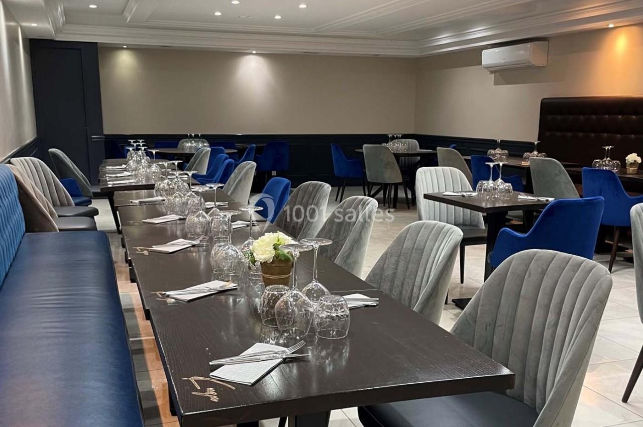 Salle de restaurant élégante avec tables dressées, chaises en velours bleu et gris, et éclairage tamisé.
