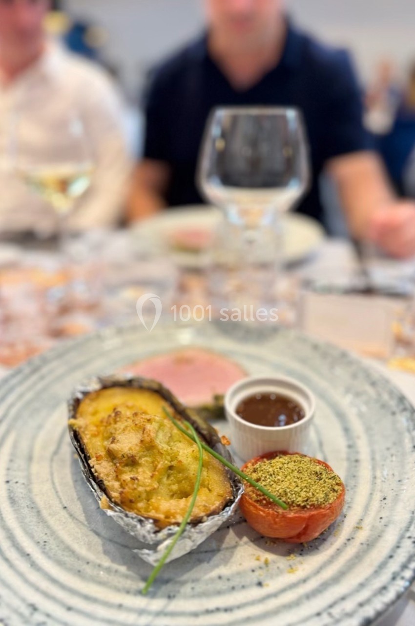 Assiette contenant un gratin en coque d'aluminium, une tomate garnie, une sauce et une garniture, sur une table dressée.