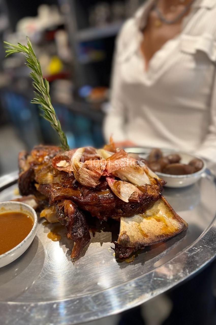 Plat de côtes de bœuf grillées garni d'oignons et romarin, accompagné de sauce et pommes de terre sur un plateau.