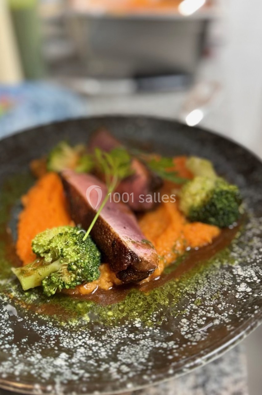 Assiette de viande grillée servie avec purée de carottes, brocolis et sauce, présentée sur une table.