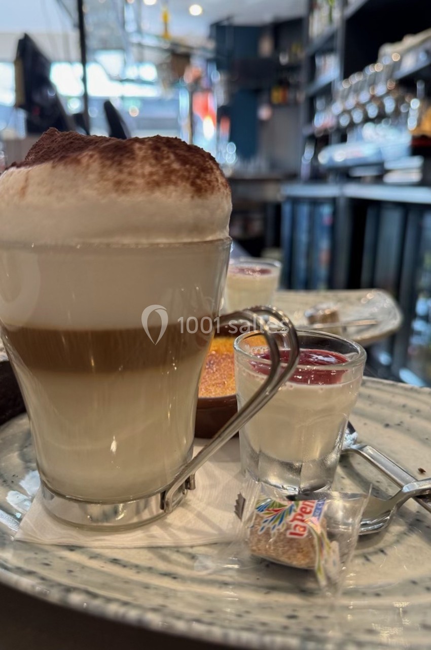 Verre de cappuccino avec mousse épaisse, accompagné de desserts et d'un sucre emballé sur une table de café.