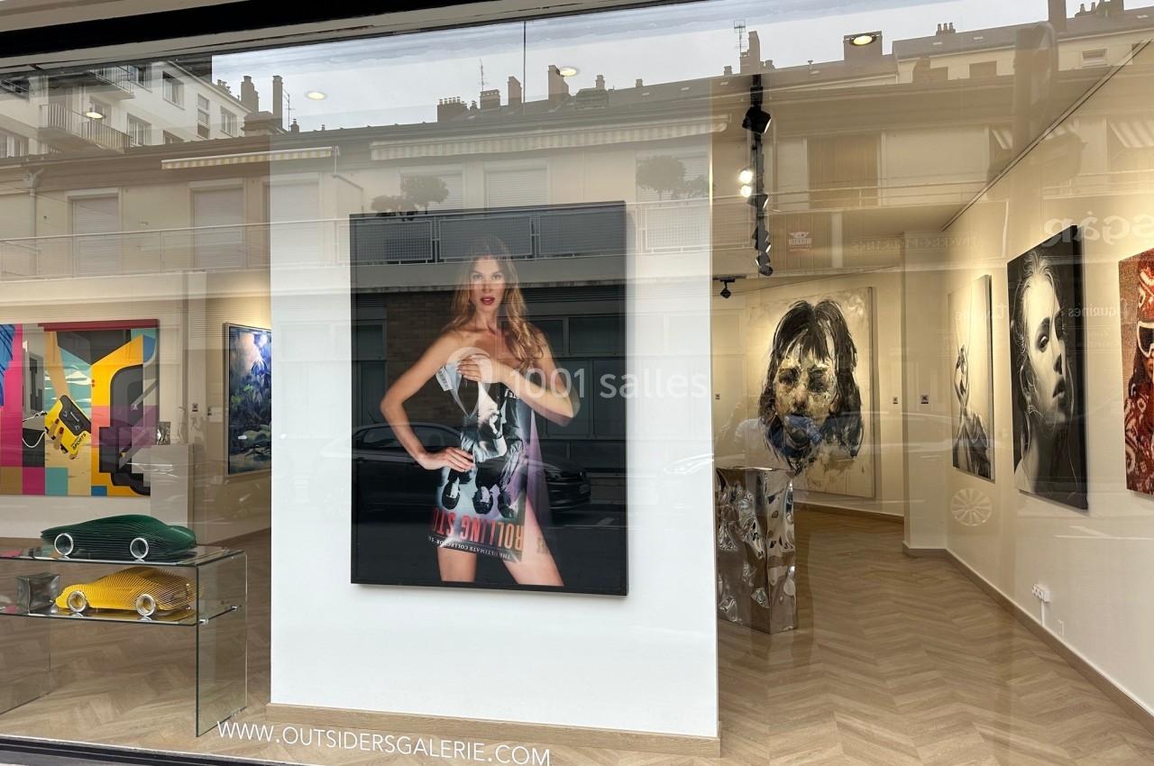 Vue d'une galerie d'art avec des œuvres contemporaines exposées, visibles à travers une vitrine en verre.