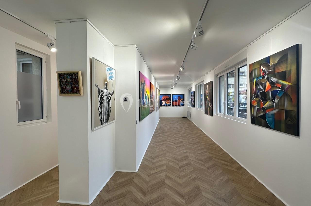 Vue intérieure d'une galerie d'art moderne avec des tableaux colorés accrochés sur des murs blancs et un sol en parquet.