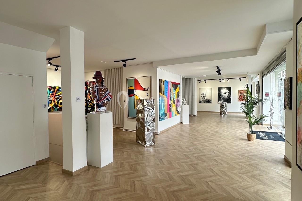 Vue intérieure d'une galerie d'art moderne avec des œuvres colorées exposées sur les murs et des sculptures au centre.