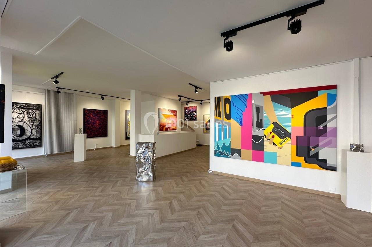 Vue d'une galerie d'art moderne avec des peintures colorées accrochées aux murs et un sol en parquet clair.