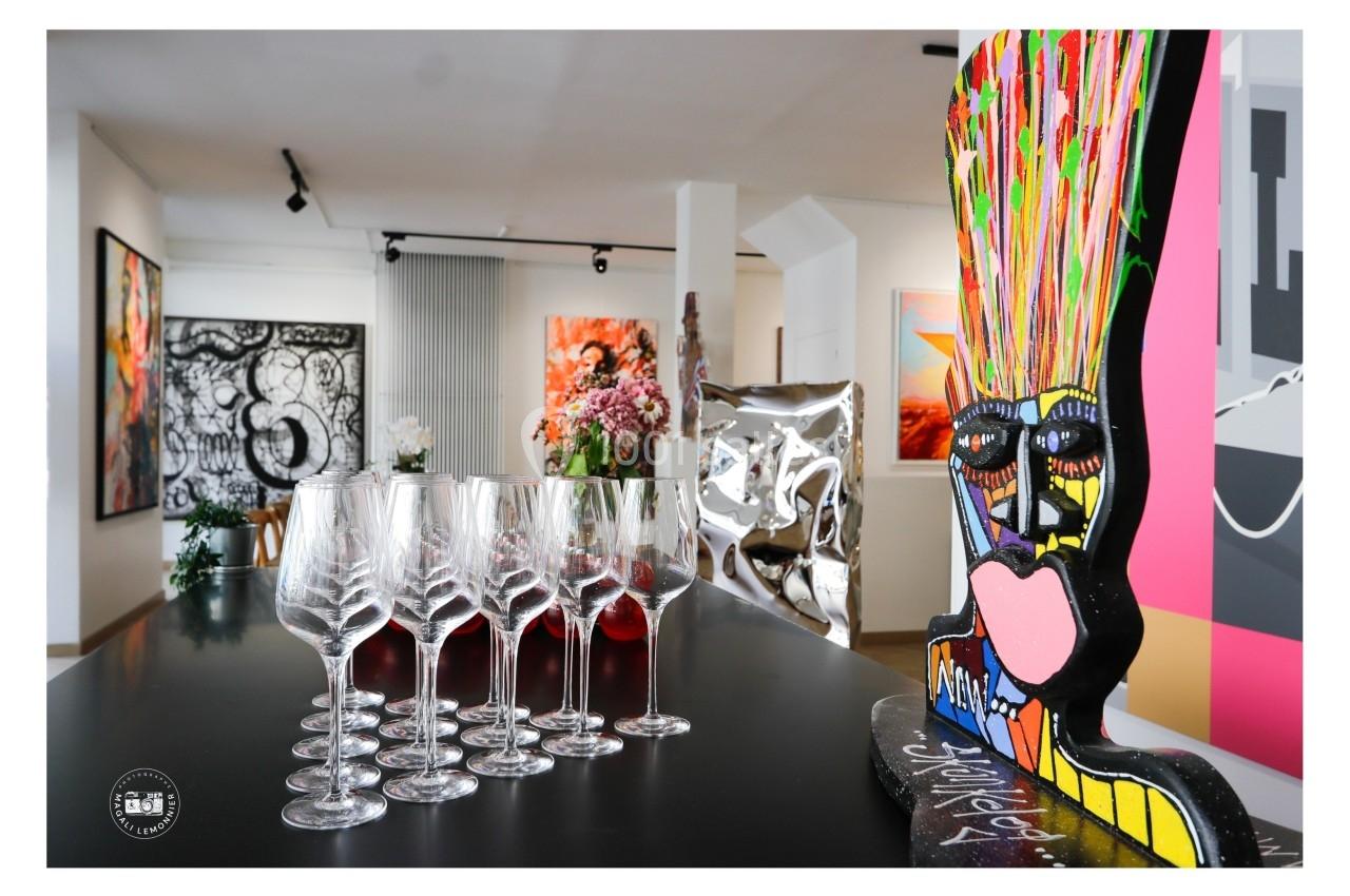 Des verres à vin alignés sur une table noire dans une galerie d'art moderne avec des œuvres colorées en arrière-plan.