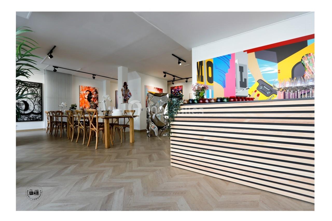 Salle lumineuse avec parquet en chevrons, table en bois, œuvres d'art modernes aux murs et comptoir à l'avant-plan.
