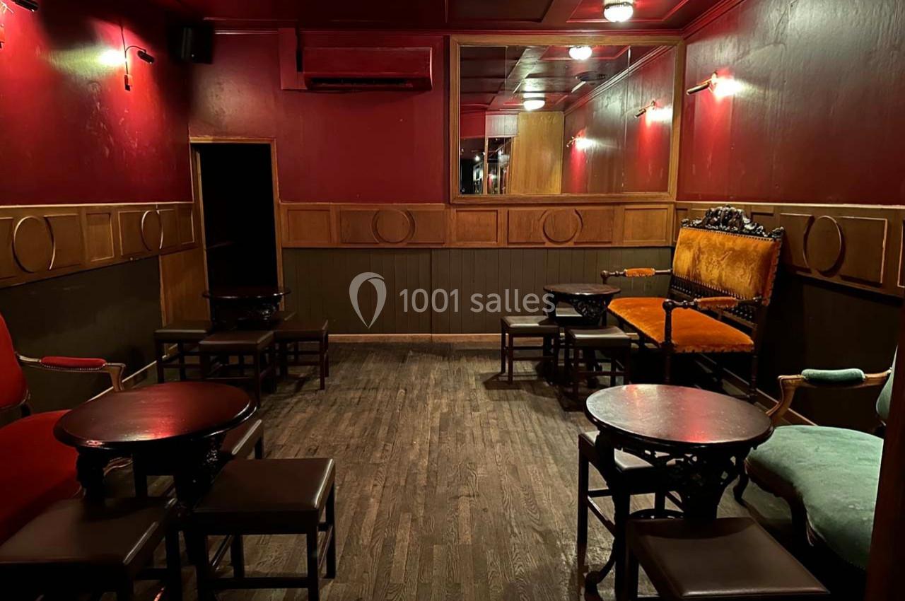 Salle intérieure avec murs rouges, mobilier en bois sombre, fauteuils colorés et éclairage tamisé.