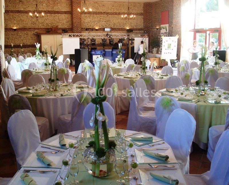 Salle de réception décorée pour un événement, avec tables rondes dressées, nappes vertes et blanches, et compositions…