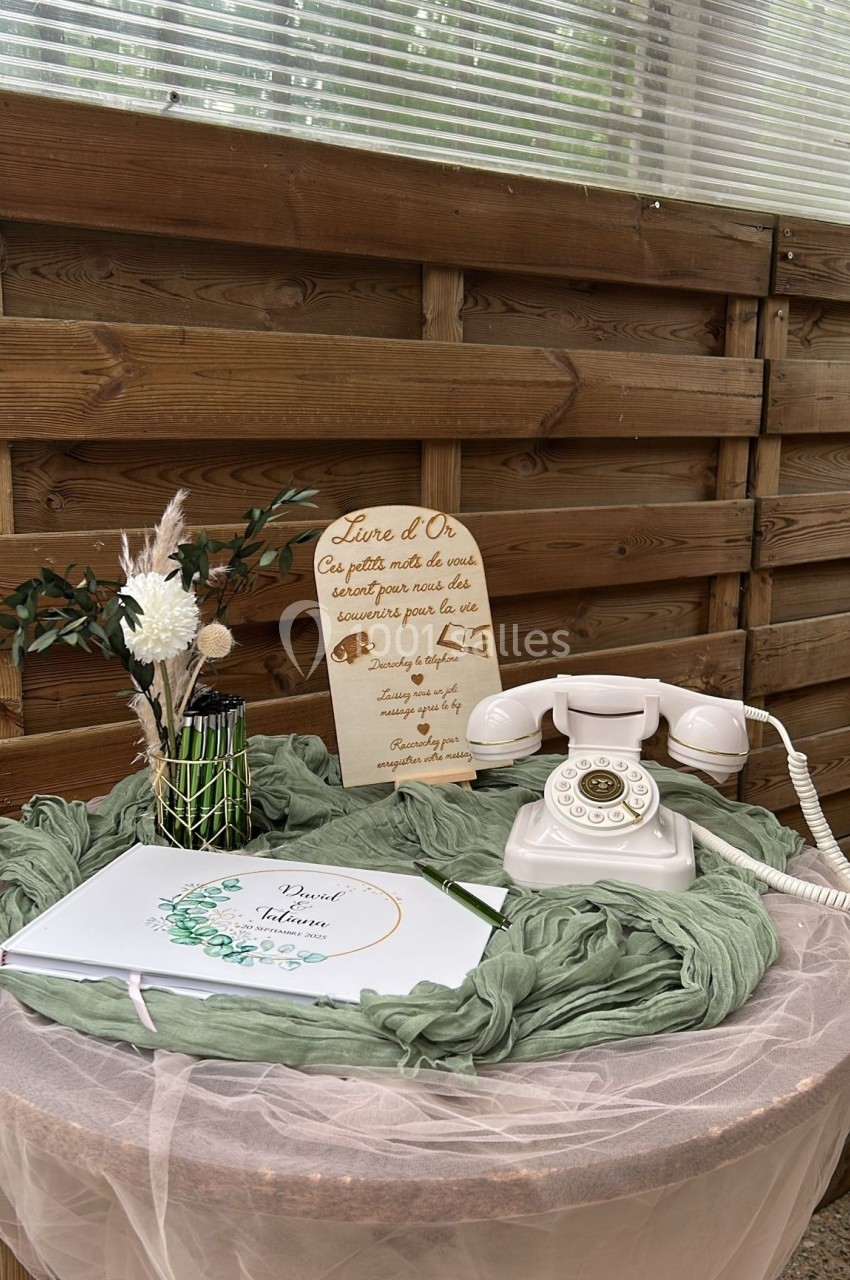 Téléphone rétro blanc, livre d'or et décoration florale sur une table ronde drapée de tissu vert et blanc.