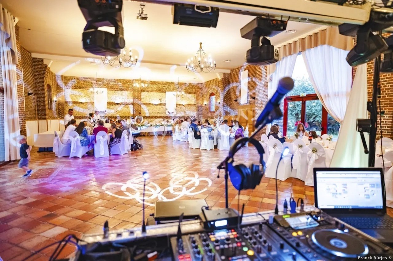 Vue d'une salle de réception avec des invités assis, éclairages décoratifs et matériel de DJ au premier plan.