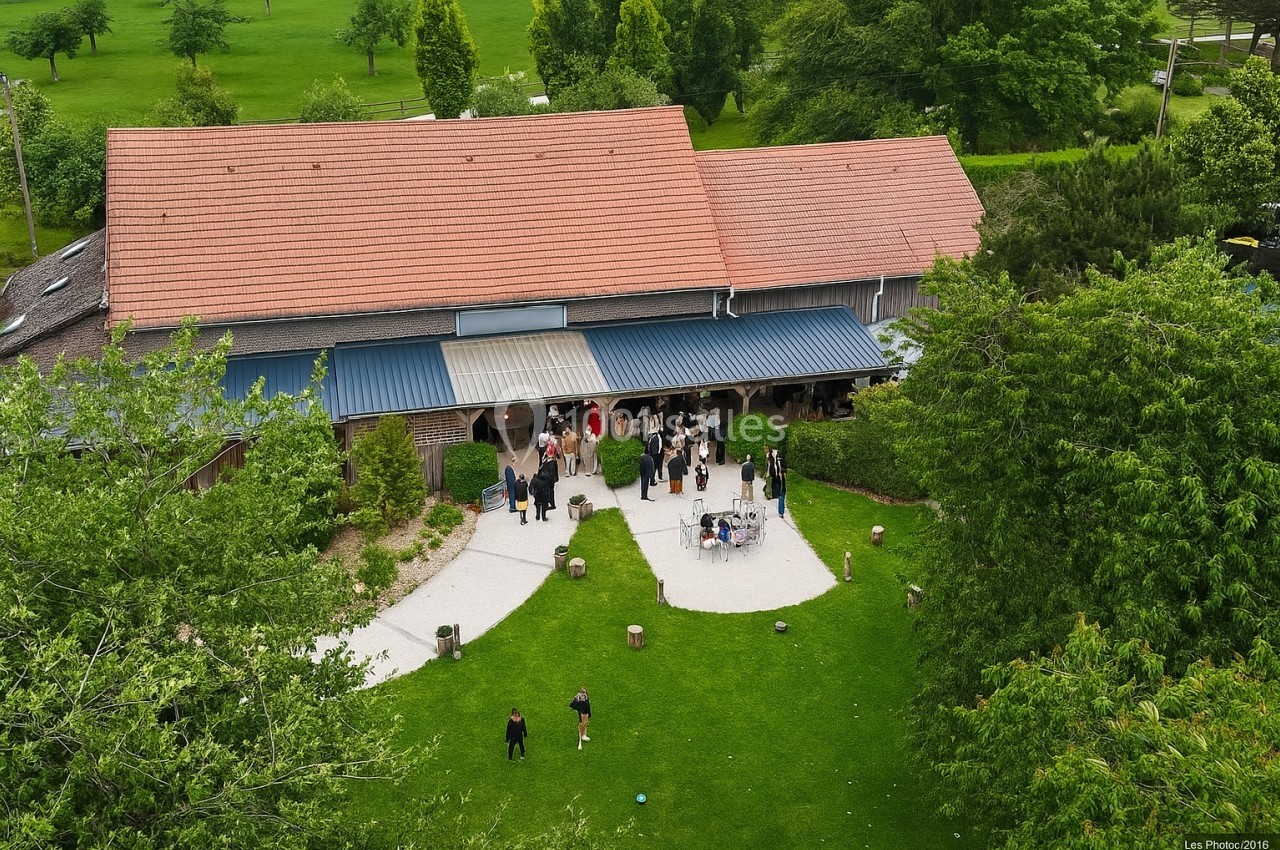Vue aérienne d'un bâtiment avec toit en tuiles entouré de verdure, des personnes rassemblées devant l'entrée.