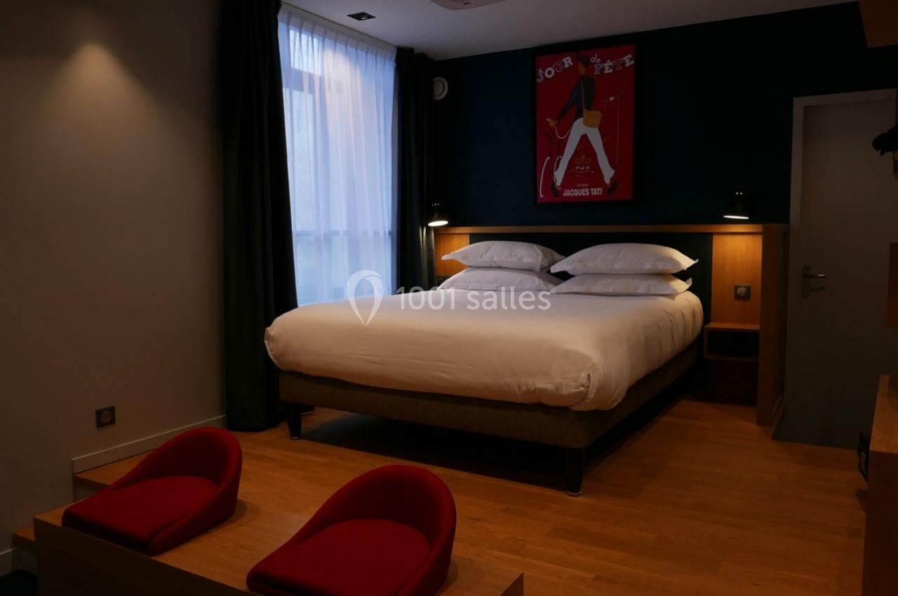 Chambre d'hôtel avec un grand lit, deux fauteuils rouges, parquet au sol et une affiche encadrée au mur.