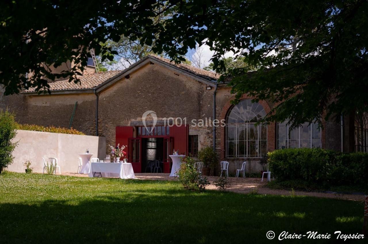 Façade d'un bâtiment ancien avec des tables dressées et des chaises dans un jardin ombragé.