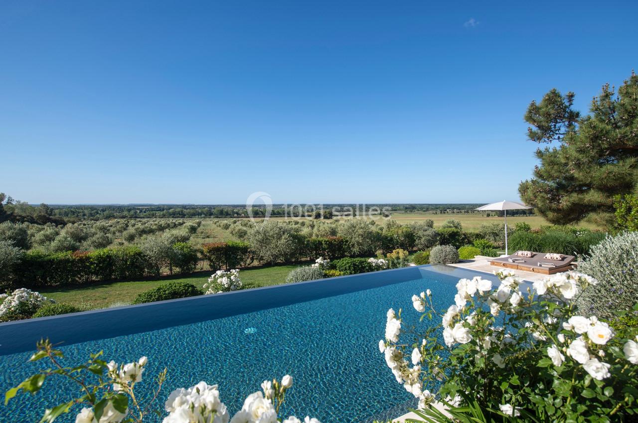 Piscine à débordement entourée de fleurs blanches, avec vue sur un paysage champêtre et ciel dégagé.
