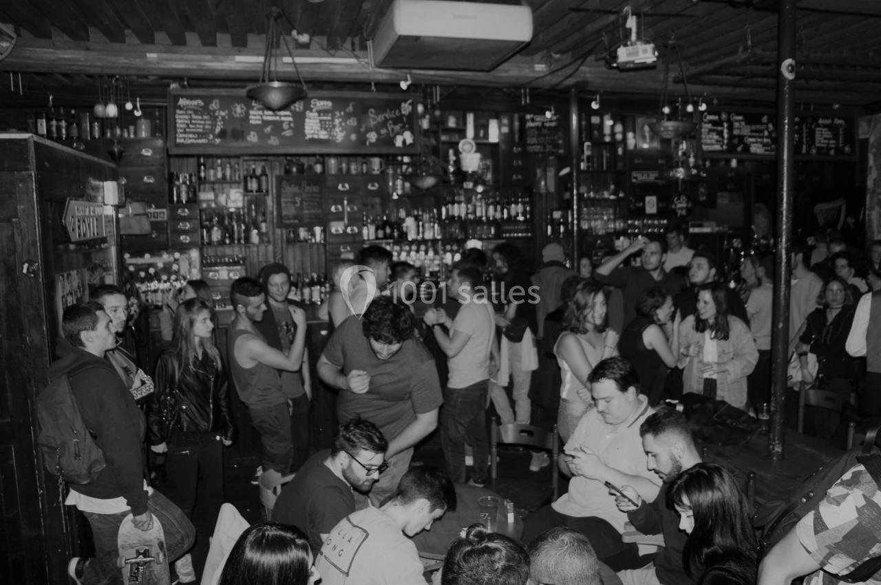 Groupe de personnes dans un bar animé, discutant et socialisant dans une ambiance conviviale en noir et blanc.