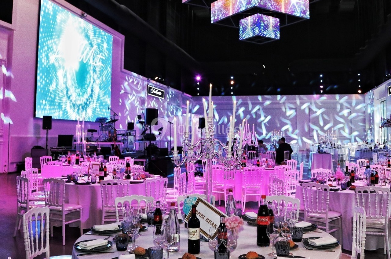 Salle de réception décorée avec des tables dressées, des chandeliers et des éclairages colorés.