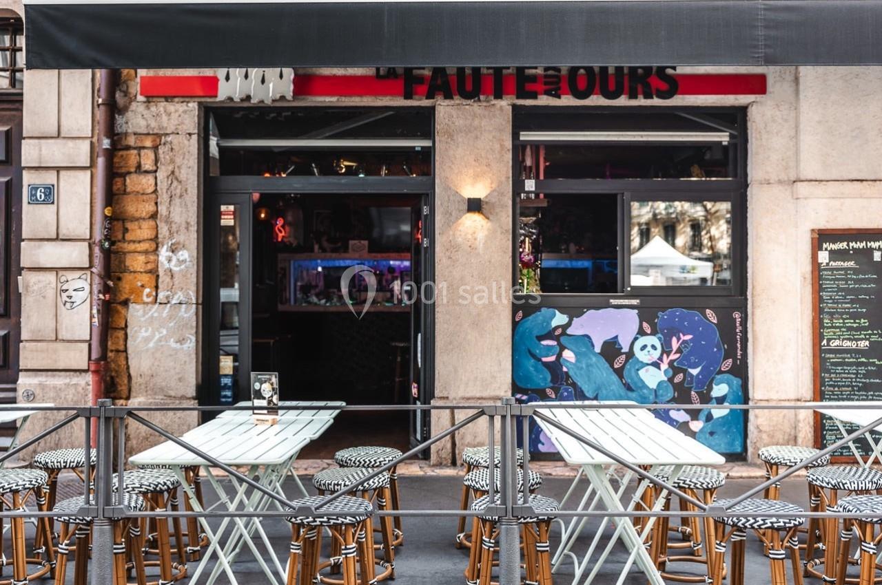 Terrasse avec tables et chaises devant un café au store noir, façade ornée de graffitis colorés.