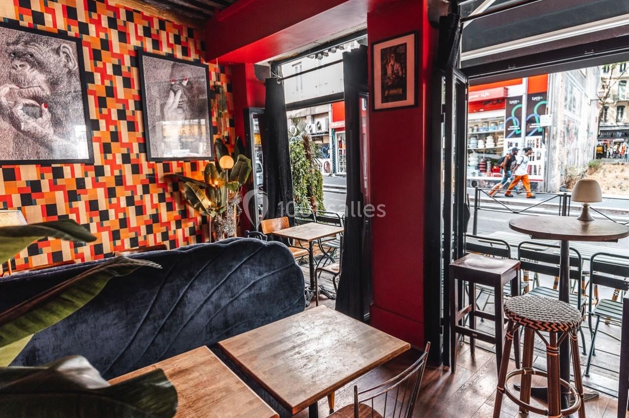 Intérieur d'un café avec mobilier en bois, banquette bleue, murs colorés et vue sur une rue animée à travers la vitrine.