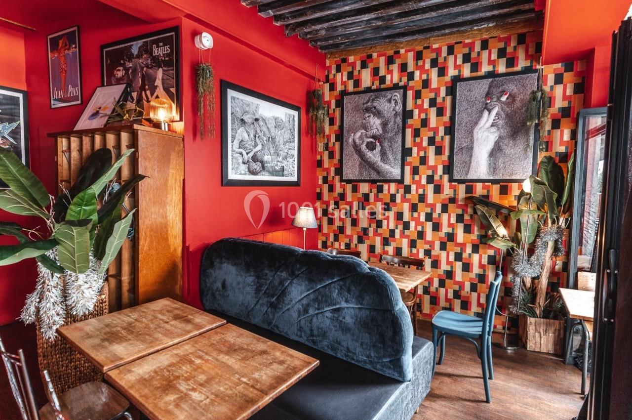 Salle de restaurant avec murs rouges et décorations artistiques, banquette bleue et tables en bois.