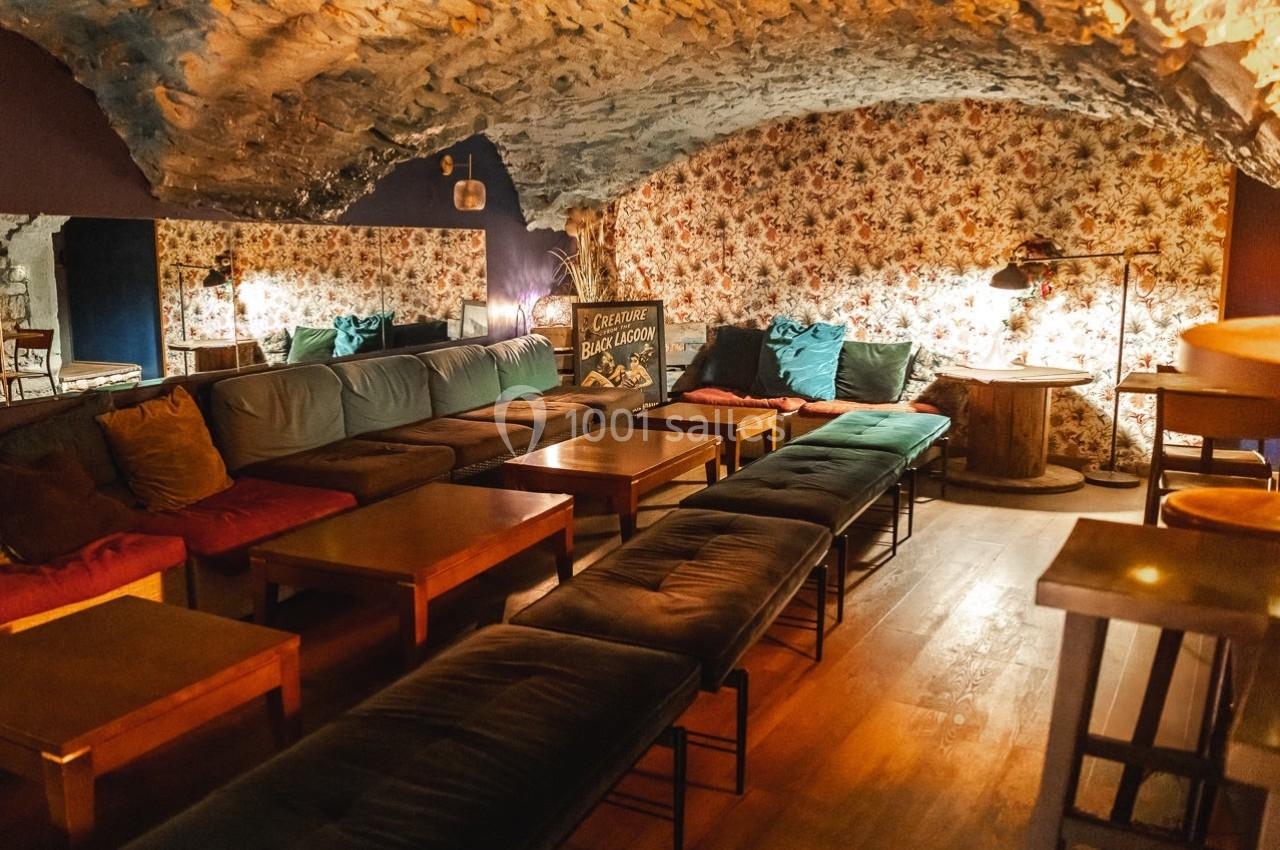 Salle voûtée avec murs en pierre, banquettes colorées, tables en bois et éclairage tamisé.