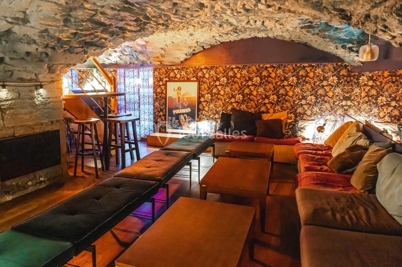 Salle voûtée avec murs en pierre, décor chaleureux, canapés, tables basses et éclairage tamisé.