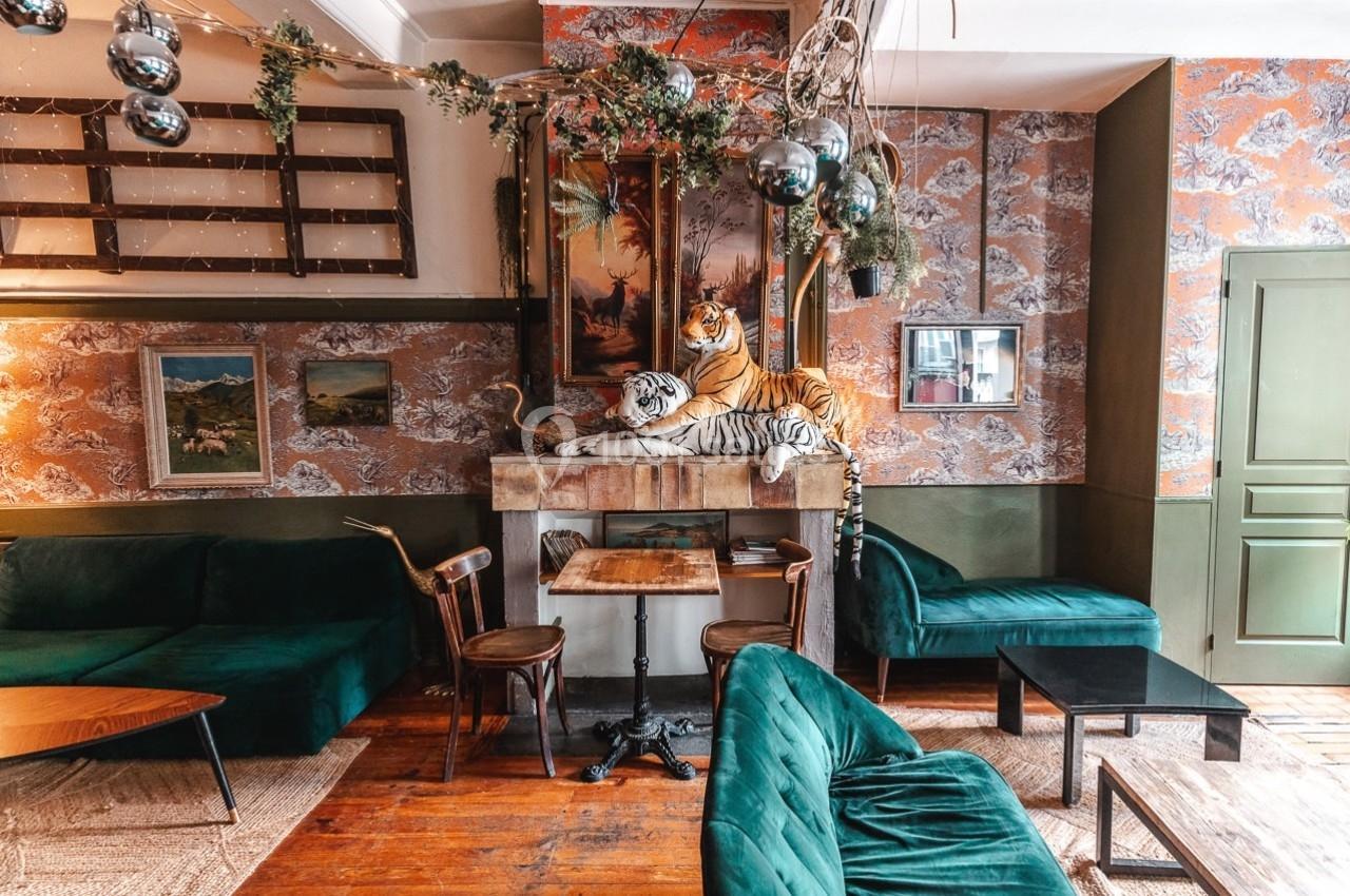 Salon décoré avec des canapés verts, des tableaux, des plantes suspendues et une sculpture de tigres sur une cheminée.