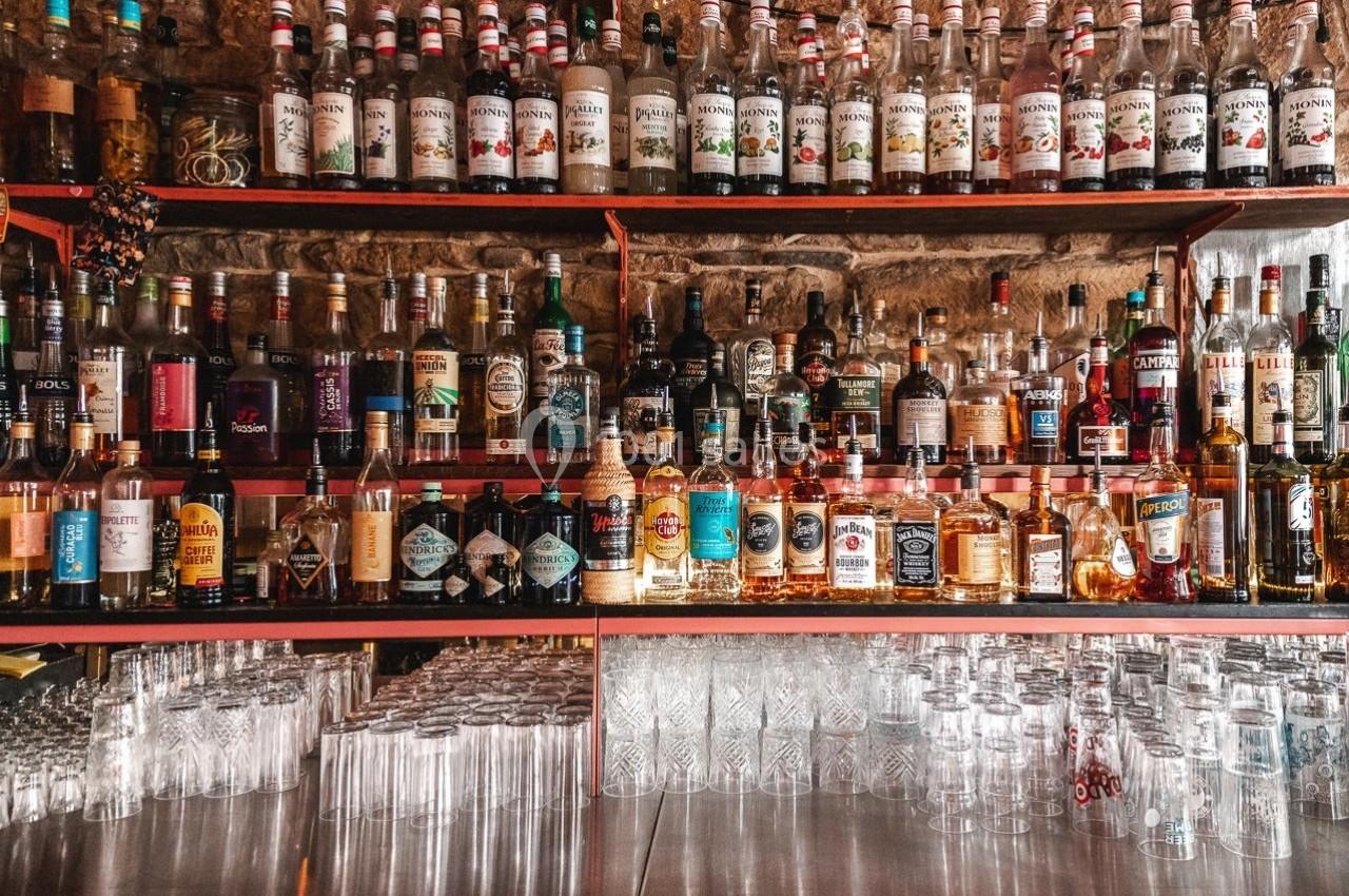 Étagères remplies de bouteilles d'alcool variées au-dessus d'un comptoir avec des verres alignés.