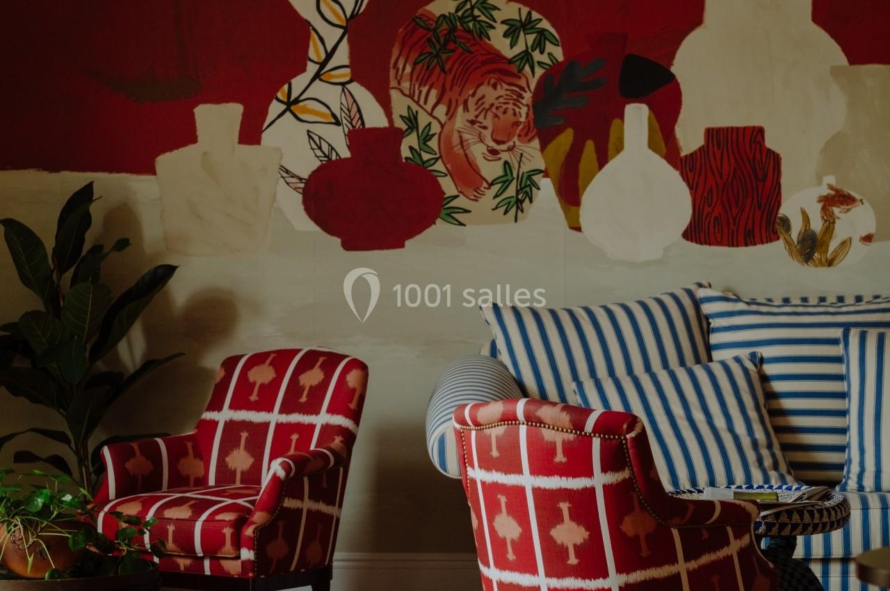Deux fauteuils rouges à motifs blancs et un canapé rayé bleu et blanc devant un mur rouge décoré de vases peints.