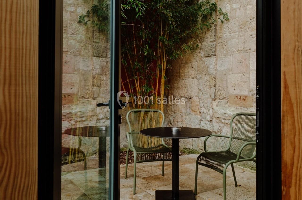 Vue d'une petite terrasse avec deux chaises vertes, une table ronde noire et des bambous en arrière-plan.