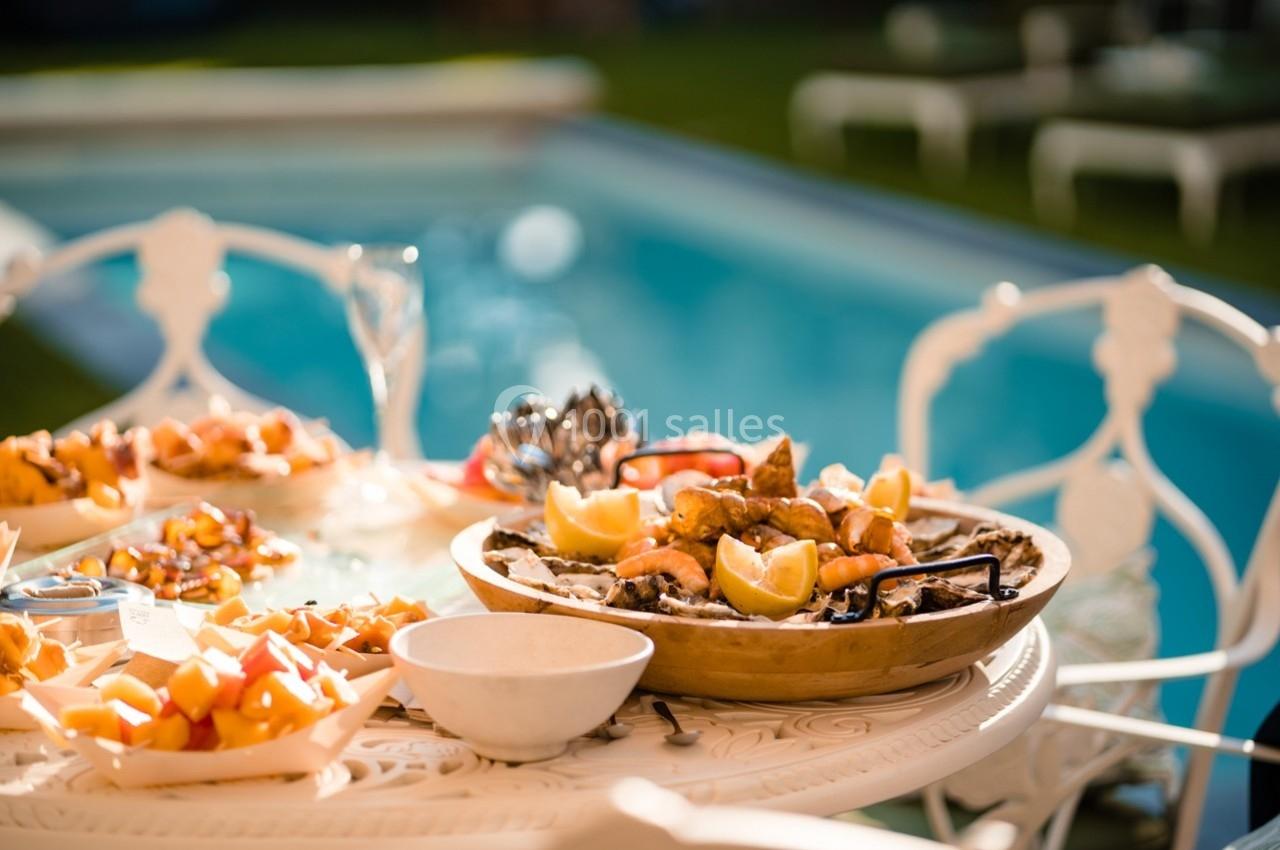 Plateau de fruits de mer et autres plats disposés sur une table blanche près d'une piscine en extérieur.