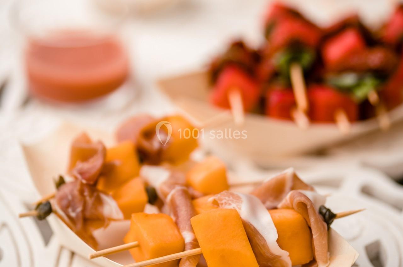 Brochettes de melon, jambon cru et mozzarella au premier plan, avec des brochettes de fraises en arrière-plan flou.
