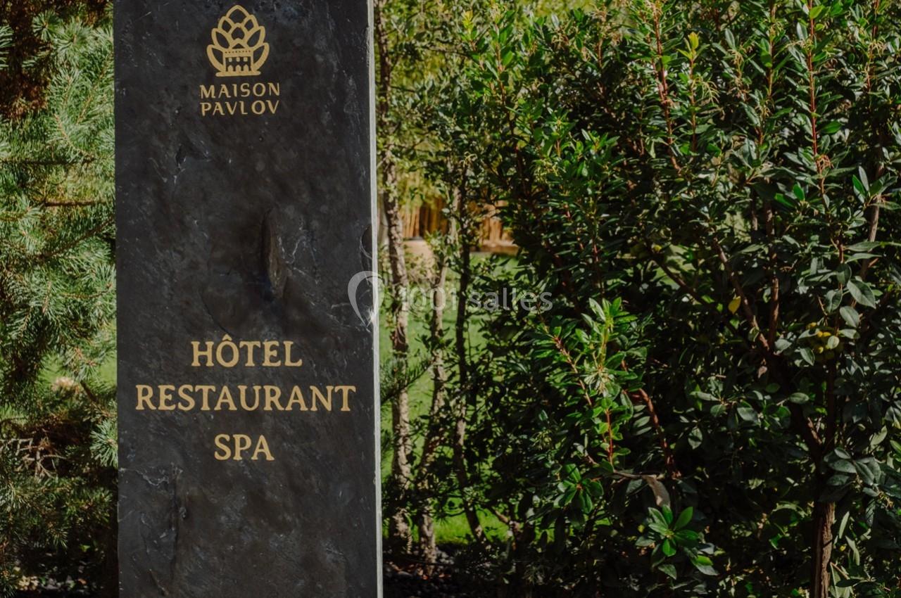 Panneau en pierre indiquant ’Hôtel Restaurant Spa Maison Pavlov’, entouré de végétation.
