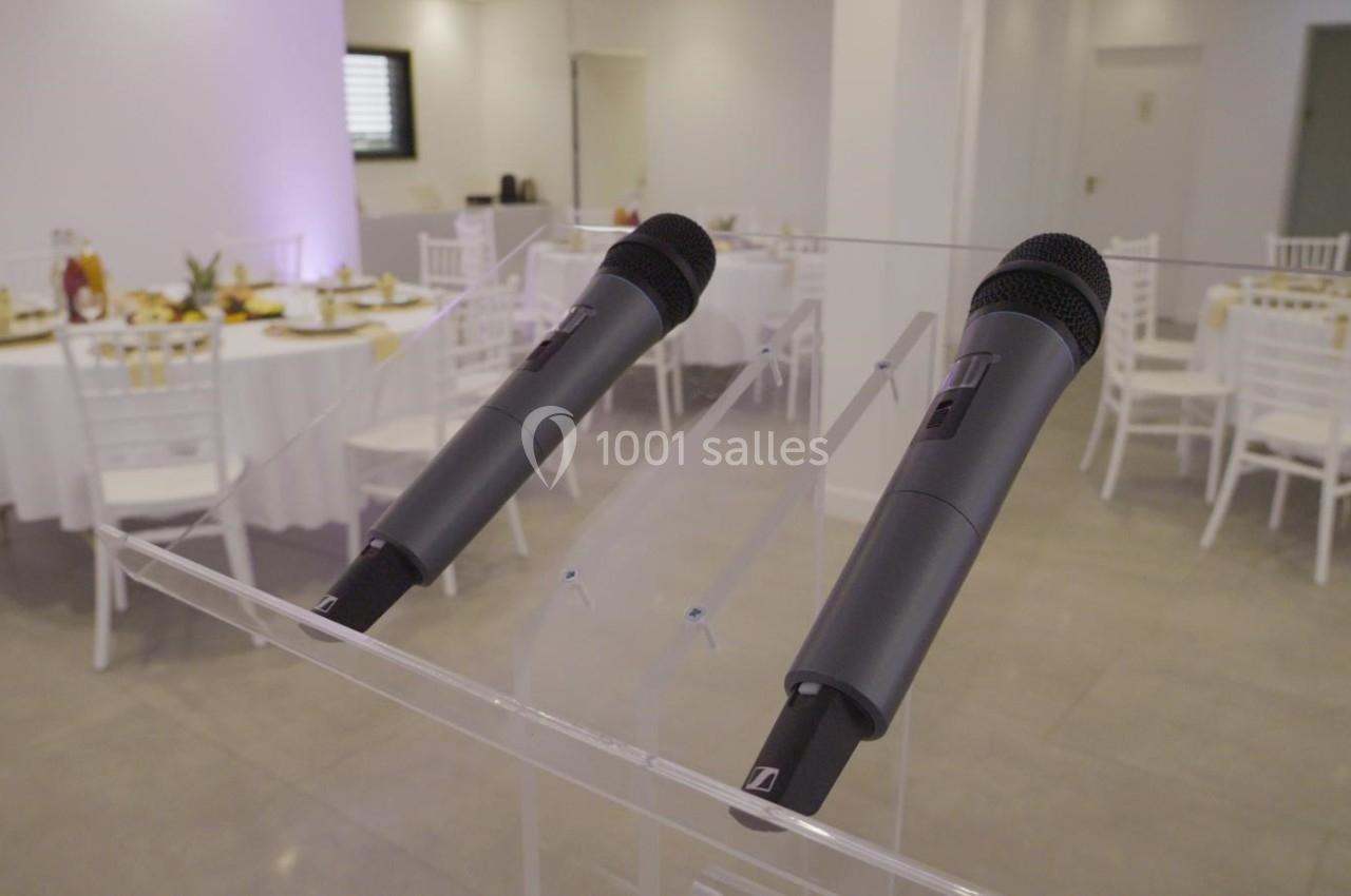 Deux microphones sans fil posés sur un pupitre transparent, avec des tables dressées en arrière-plan.