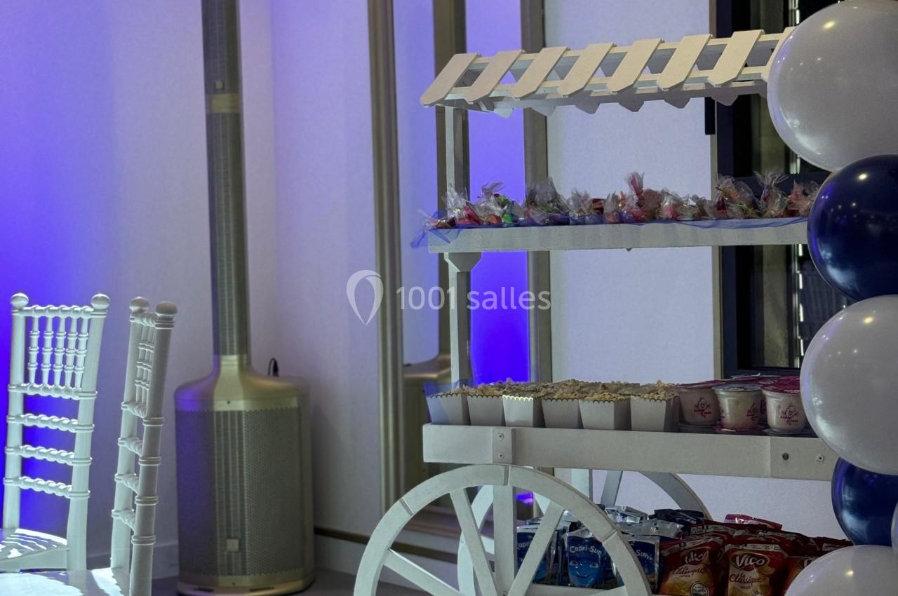 Chariot blanc décoratif avec friandises, entouré de ballons et d'une chaise blanche dans une salle éclairée en bleu.