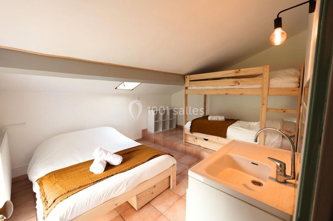 Chambre mansardée avec lit double, lits superposés en bois, lavabo et lumière naturelle provenant d'une fenêtre de toit.
