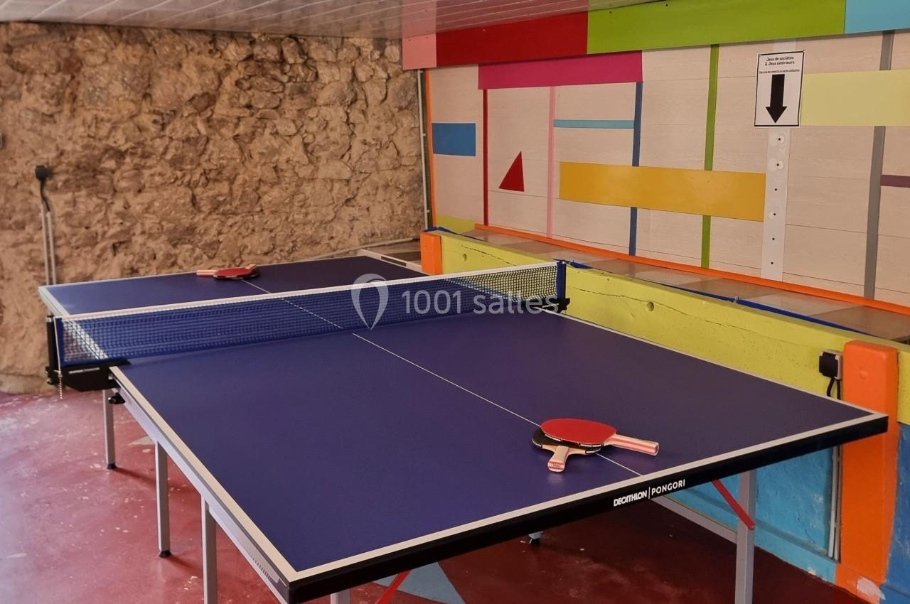 Table de ping-pong avec deux raquettes rouges posées, dans une pièce colorée aux murs en pierre et décorés de motifs…