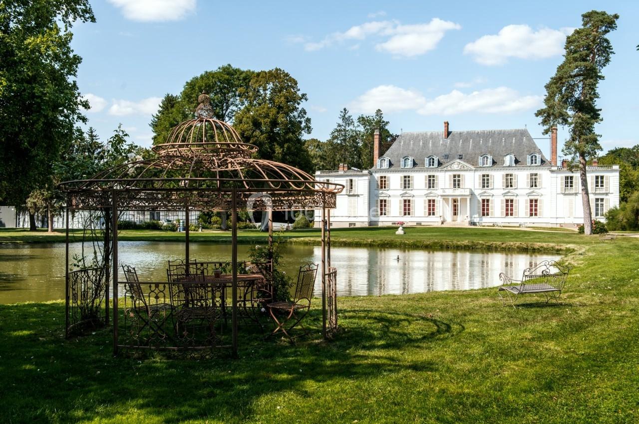 Pavillon en fer forgé près d'un étang, avec un manoir blanc en arrière-plan entouré de verdure.