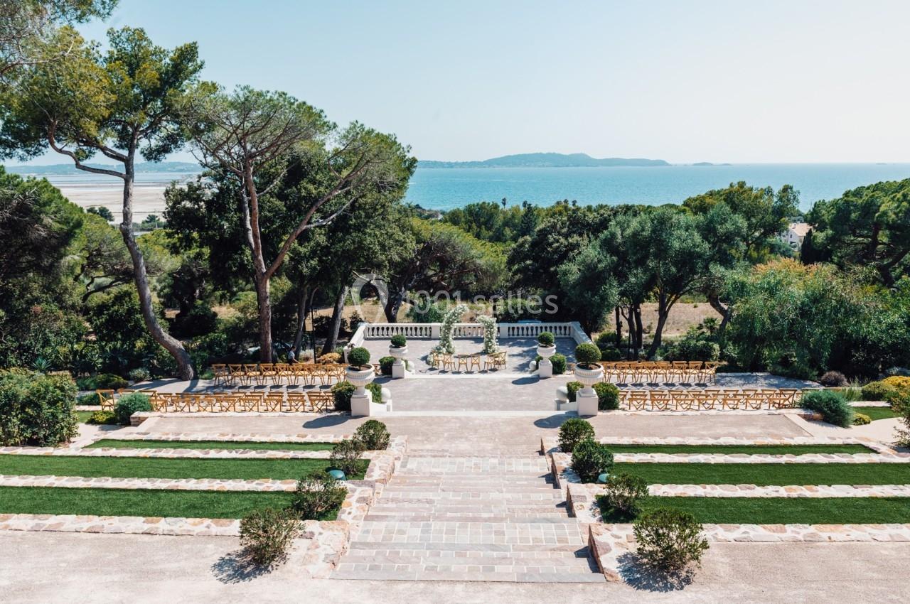Jardin en terrasses avec vue sur la mer, disposant de chaises alignées pour un événement en plein air.
