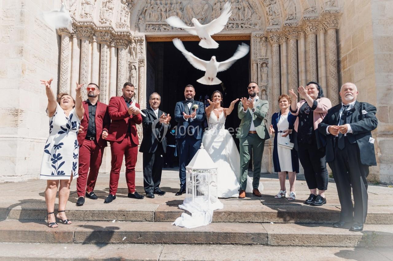 Un couple de mariés et leurs invités devant une église libèrent des colombes en signe de célébration.