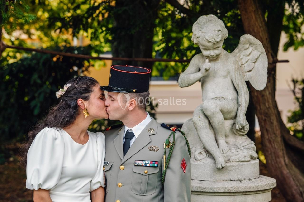 Un couple s'embrasse devant une statue d'ange dans un jardin arboré.