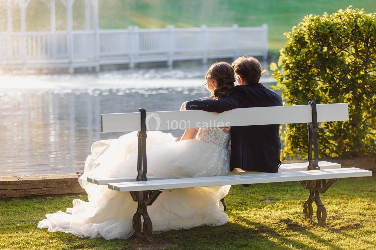 Un couple assis sur un banc près d'un étang, regardant l'eau sous une lumière douce en fin de journée.